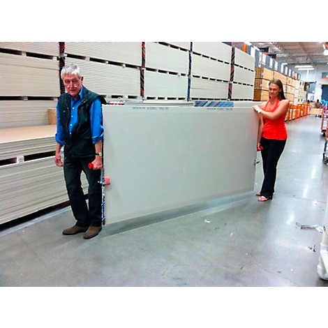 A man and woman carrying a large drywall sheet together in a hardware store.