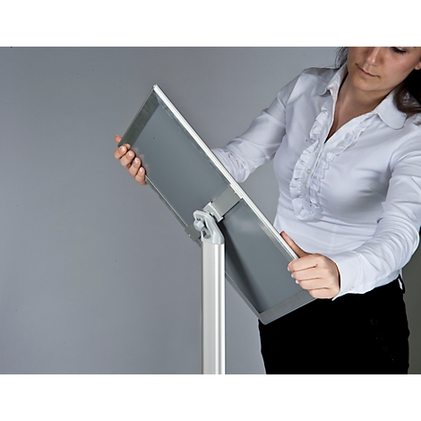 Woman holding a white and gray presentation board. She wears a white shirt and black pants.