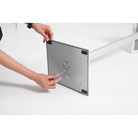 Person assembling product part with wrench. Square metal plate, four rubber feet, silver tube.
