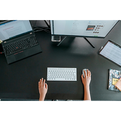 Vue de dessus d'un bureau avec un ordinateur portable, un moniteur, un clavier et des mains utilisant une souris.