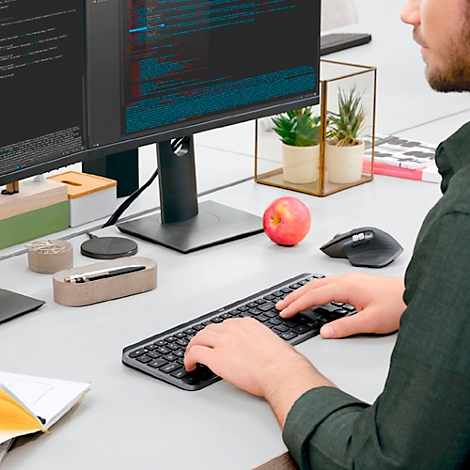 Une personne tape sur un clavier. Des fruits, une souris et des accessoires de bureau sont sur le bureau.