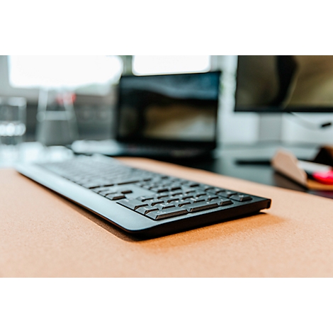Clavier noir sur une surface brun clair. En arrière-plan, un ordinateur portable et un moniteur flous.