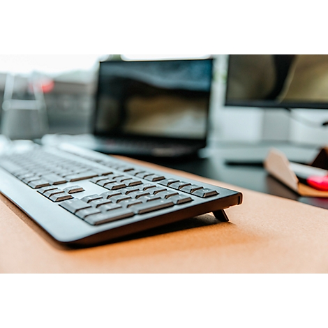 Clavier sur une surface de table marron, ordinateur portable et moniteur derrière.