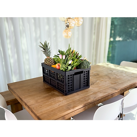 Black crate with fruits and vegetables on a wooden table. Pineapple, tulips and broccoli are recognizable.