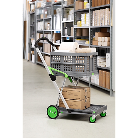 A gray folding cart with green accents, loaded with boxes and roll paper, stands in a warehouse shelf.