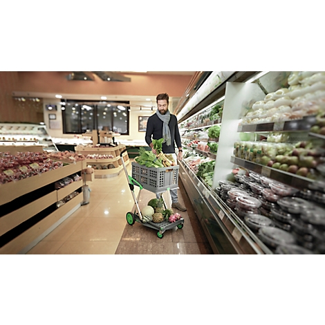 Man in a supermarket with a shopping cart filled with vegetables. He is standing in front of a refrigerated section with vegetables.
