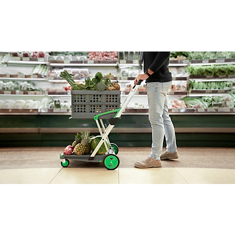 Person pushing a shopping cart filled with fruits and vegetables in a supermarket. Shelves in the background.