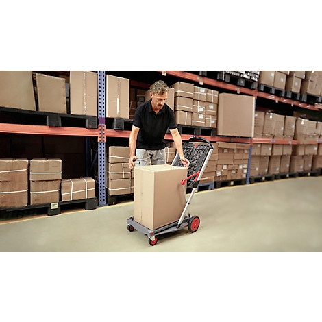 A man loads a trolley with a cardboard box in a warehouse. Shelves are visible in the background.