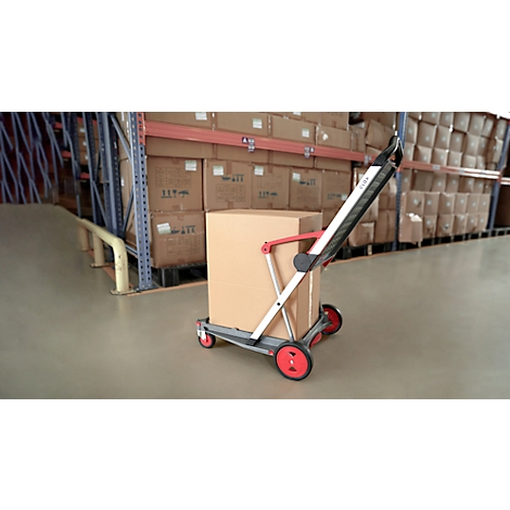 Hand truck with box in warehouse. Red wheels, gray frame.