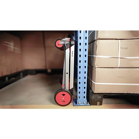 A folded red and silver scooter stands between a blue metal shelf and boxes.