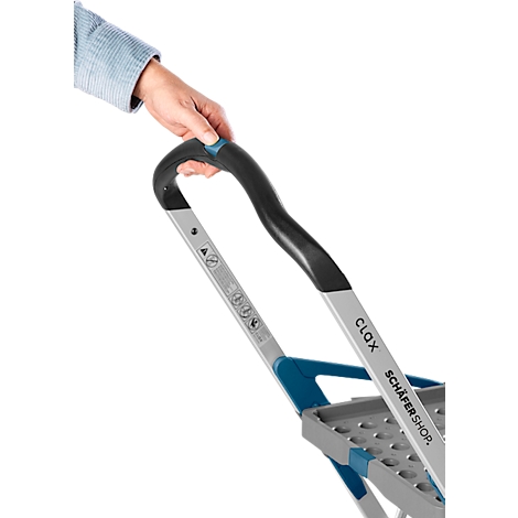 Eine Hand greift den schwarzen Griff eines grau-blauen Rollwagens. Auf der Stange ist "CLAX SCHÄFER SHOP" zu lesen.