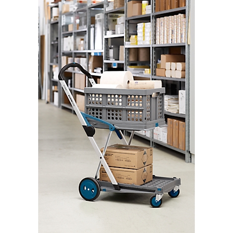 Grauer Einkaufswagen mit blauen Rädern, gefüllt mit Kartons und Rollen. Regale im Hintergrund.