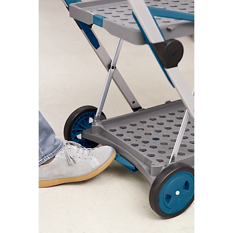 Ein Fuß betätigt einen blauen Hebel an einem grauen Trolley. Der Trolley hat blaue Akzente und schwarze Räder.