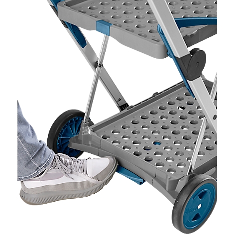 Gros plan d'un chariot de service pliable gris. Un pied actionne le frein au pied. Les roues sont noires et bleues.