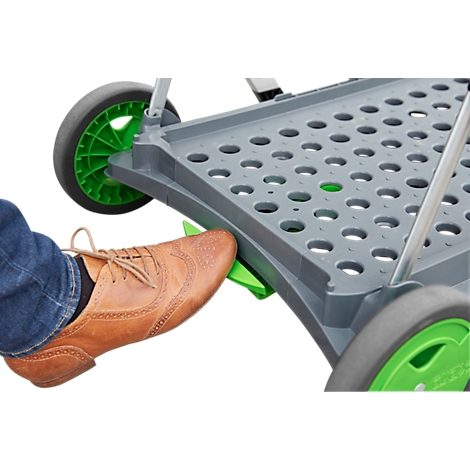 Primer plano de un zapato marrón pisando un pedal verde en un carro gris plegable con ruedas verdes.