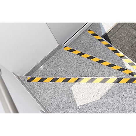 Staircase with yellow and black warning stripes, grey floor, light wall. The warning stripes mark the edges of the stairs.