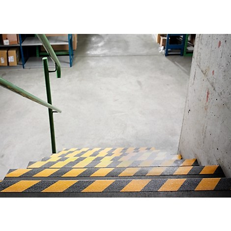 Stairs with yellow and black warning stripes and a green handrail. Concrete wall on the right.