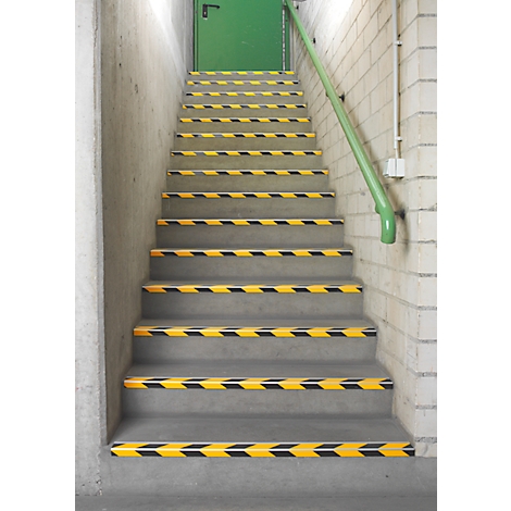 Staircase with yellow and black warning stripes, green handrail, green door.