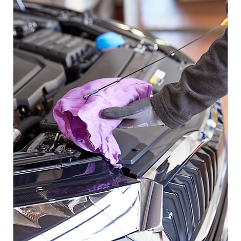 A mechanic checks the oil level of a car. He holds a pink cloth and an oil dipstick.