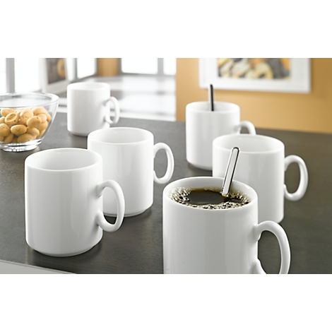 White coffee cups on a table. One cup with coffee, one with a spoon, nuts in a glass bowl.