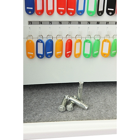 Plusieurs chevilles métalliques posées au fond d'une armoire à clés sous des porte-clés numérotés.