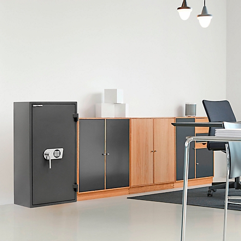 Un coffre-fort noir se trouve devant un fond de bureau. Le coffre-fort a un pavé numérique et une clé. Des armoires et un bureau sont à l'arrière-plan.