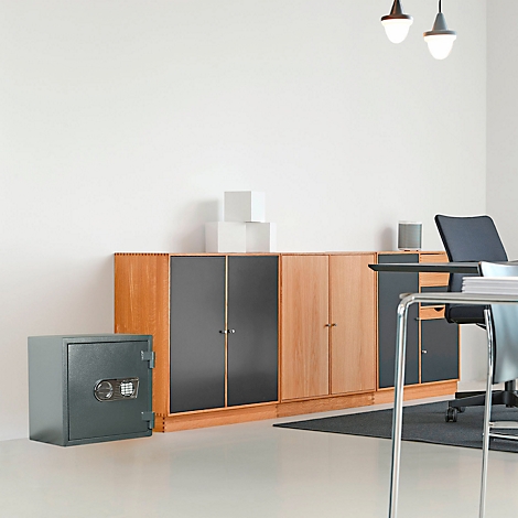Coffre-fort gris dans un bureau, à côté d'un mur d'armoires en bois, d'un bureau et d'une chaise.