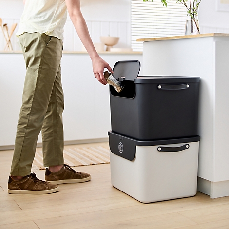 Boîte de rangement grise avec couvercle et poignées. Le couvercle est partiellement ouvert. Une découpe à droite.