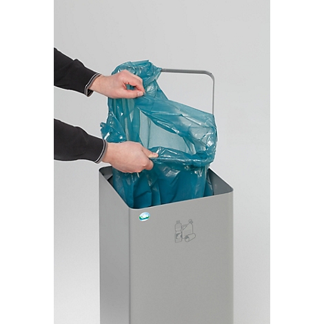 Des mains placent un sac poubelle bleu dans une poubelle grise.