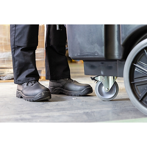 Gros plan : personne en pantalon noir et bottes debout à côté d'un chariot noir avec une roue grise.