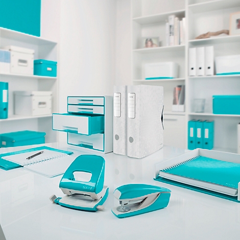 Büro mit weißem Schreibtisch, Türkis-Accessoires: Locher, Tacker, Ringbücher, Notizbuch, Ablage, Kisten, Bücher. Helle, freundliche Atmosphäre.
