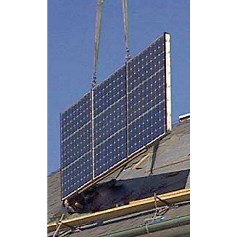 Un grand panneau solaire est installé sur un toit par une grue.