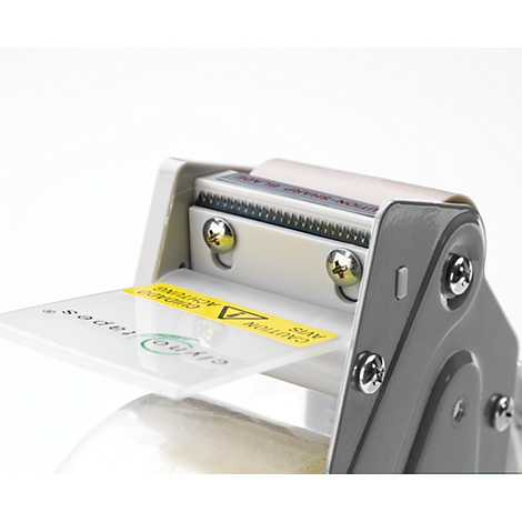 Close-up of a tape dispenser. A yellow sticker with "CAUTION" is on the plate. The device is gray and white.