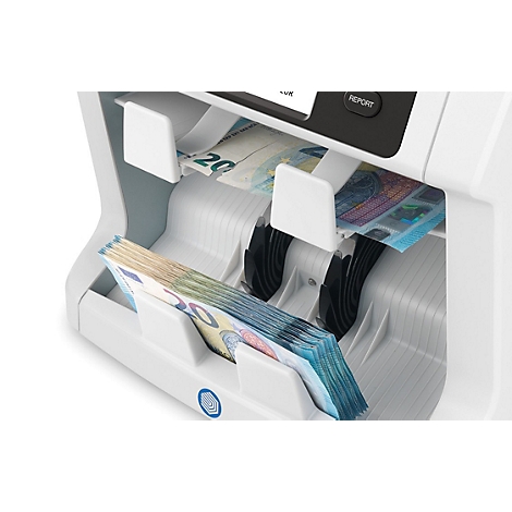 Machine de comptage de billets. Plusieurs liasses de billets et billets individuels dans le bac de sortie. Des billets de différentes coupures sont visibles sur la machine.