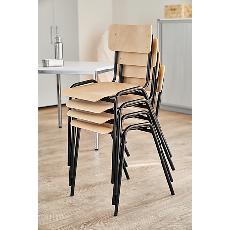 Stacked chairs with wooden seats and backs, black framed, stand in a bright room.