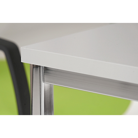 Close-up: White table top with metal legs and green background, part of a chair visible.