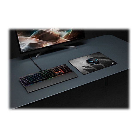 Ein Gaming-Setup mit beleuchteter Tastatur, Maus, Mauspad und Monitor auf einem dunklen Schreibtisch.
