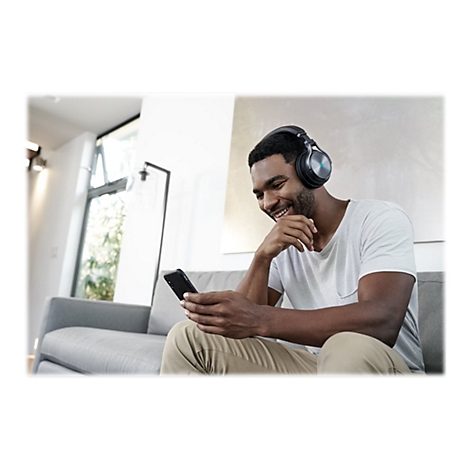 Ein Mann mit Kopfhörern sitzt auf einem Sofa, lächelt und schaut auf sein Smartphone.