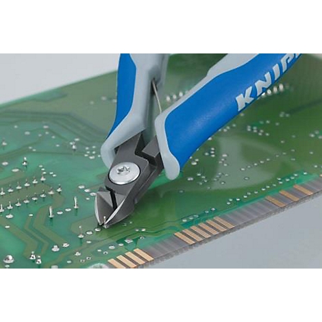 Des pinces coupantes bleues et grises coupent un fil sur une carte de circuit imprimé verte.