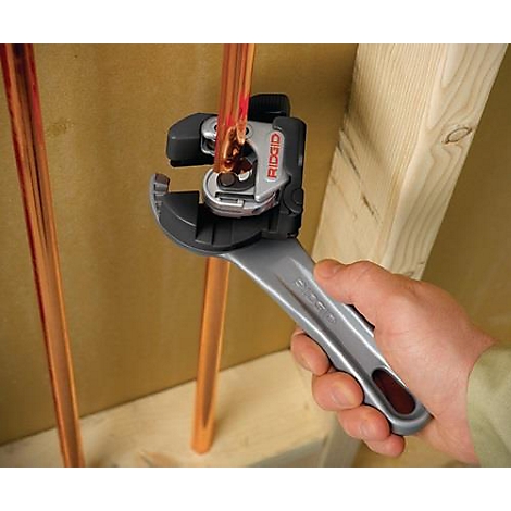 Une main utilise un coupe-tube pour couper un tuyau en cuivre. Le coupe-tube a une poignée argentée et le logo "RIDGID".