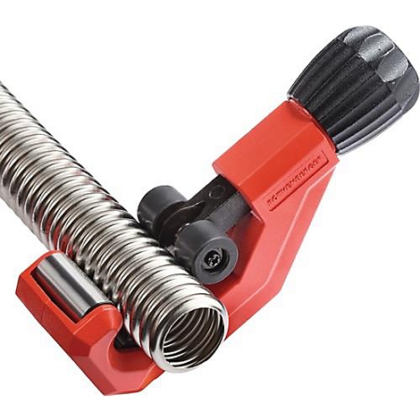 Un coupe-tube rouge coupant un tuyau ondulé argenté. L'outil a une poignée rotative noire.