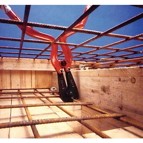 Pince à lier les fils rouges attachant des barres d'armature dans un coffrage en bois.