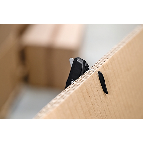 Un couteau de sécurité noir coupant à travers un morceau de carton ondulé épais.
