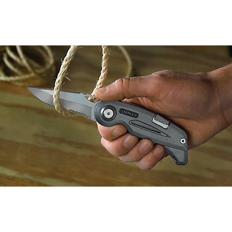 Un couteau pliant gris coupe une corde. La main tient le couteau. Une bobine de corde est en arrière-plan.