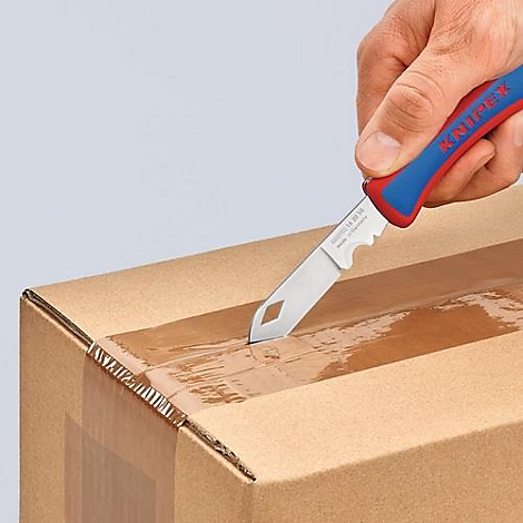 Une main coupe un carton avec un couteau KNIPEX rouge et bleu.
