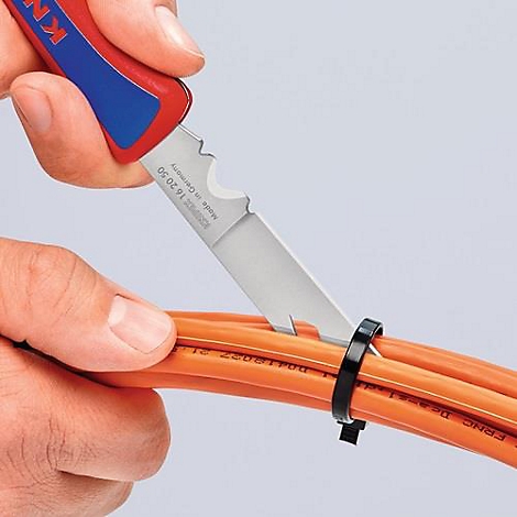 Gros plan d'une main coupant un serre-câble sur un câble orange avec un couteau.