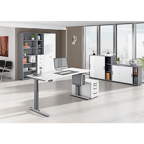 Modern white height-adjustable desk in an office. Cabinets in the background, a window with a view.