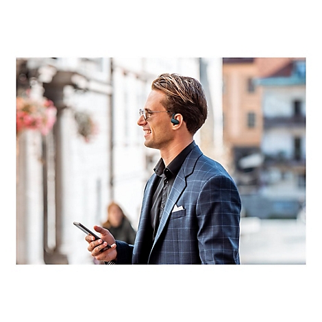 Ein Mann mit Brille und KopfhÃ¶rern lÃ¤chelt, wÃ¤hrend er ein Smartphone hÃ¤lt. Er trÃ¤gt einen Anzug, im Hintergrund eine Stadt.
