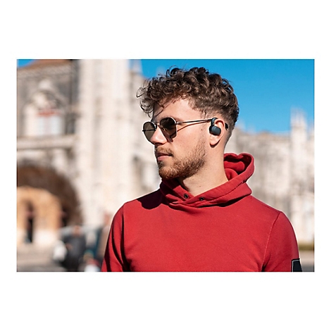 Mann mit Sonnenbrille und KopfhÃ¶rern, roter Hoodie. Im Hintergrund GebÃ¤ude und blauer Himmel.