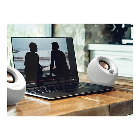 Zwei weiße Lautsprecher neben einem Laptop, auf dem ein Video abgespielt wird. Auf einem Holztisch platziert.